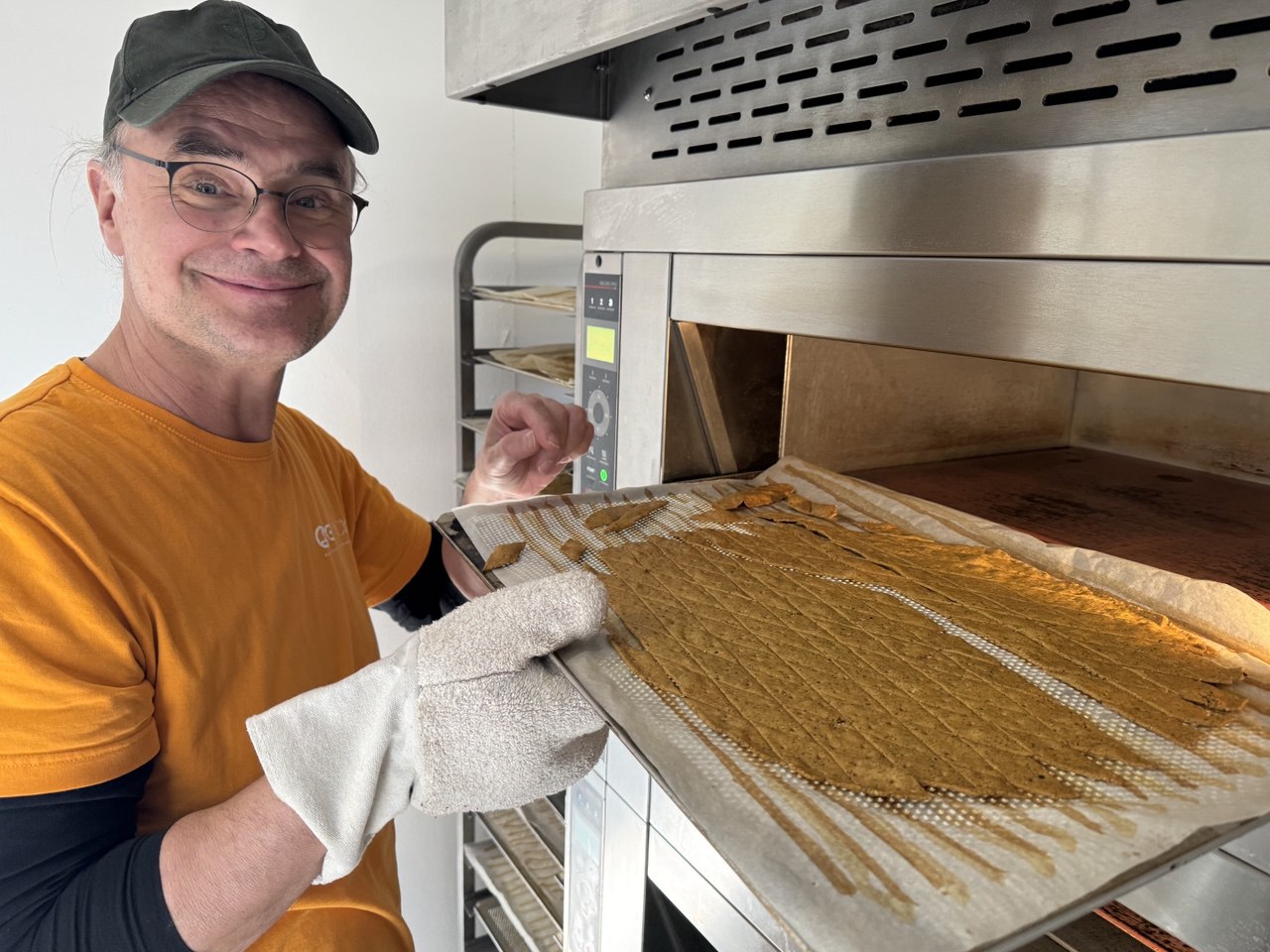Matthias Quendt, Gründer von QiO Food, präsentiert lächelnd ein Blech frisch gebackener Bio-Cracker direkt am Manufaktur-Ofen in Liemehna – ein Symbol für echtes Handwerk und persönliche Qualitätshaftung.