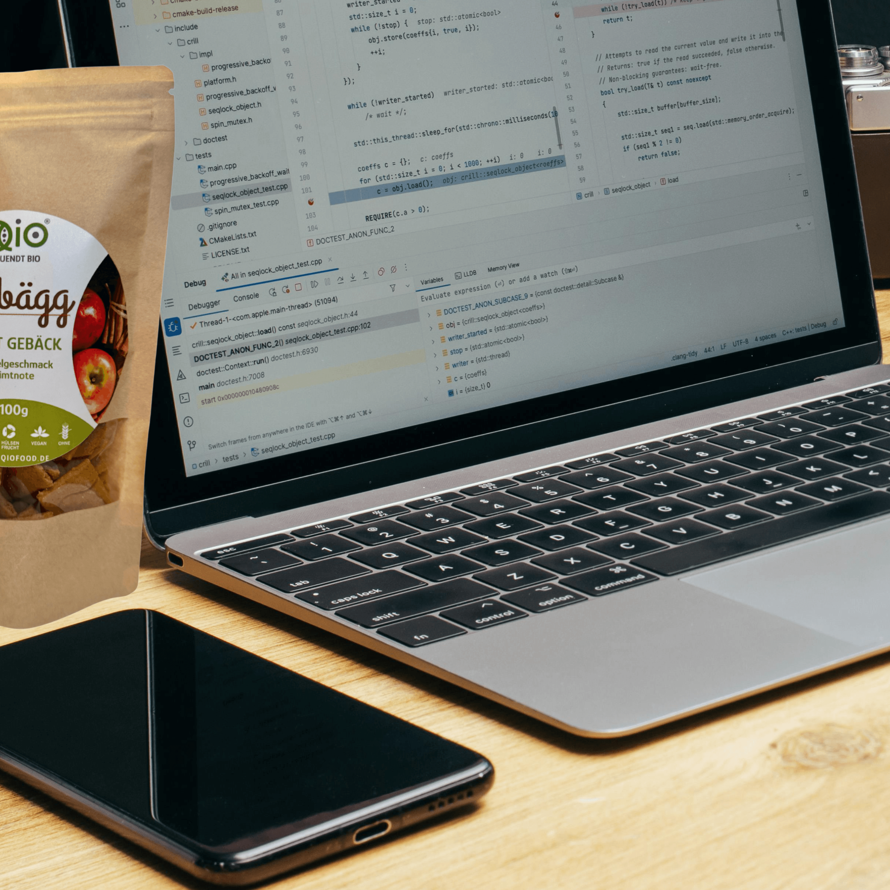Ein Laptop mit Programmcode, ein Smartphone und eine Packung QiO Gebäck Apfelzimt auf einem Holzschreibtisch bereit für Online-Beratung von Heike Quendt.